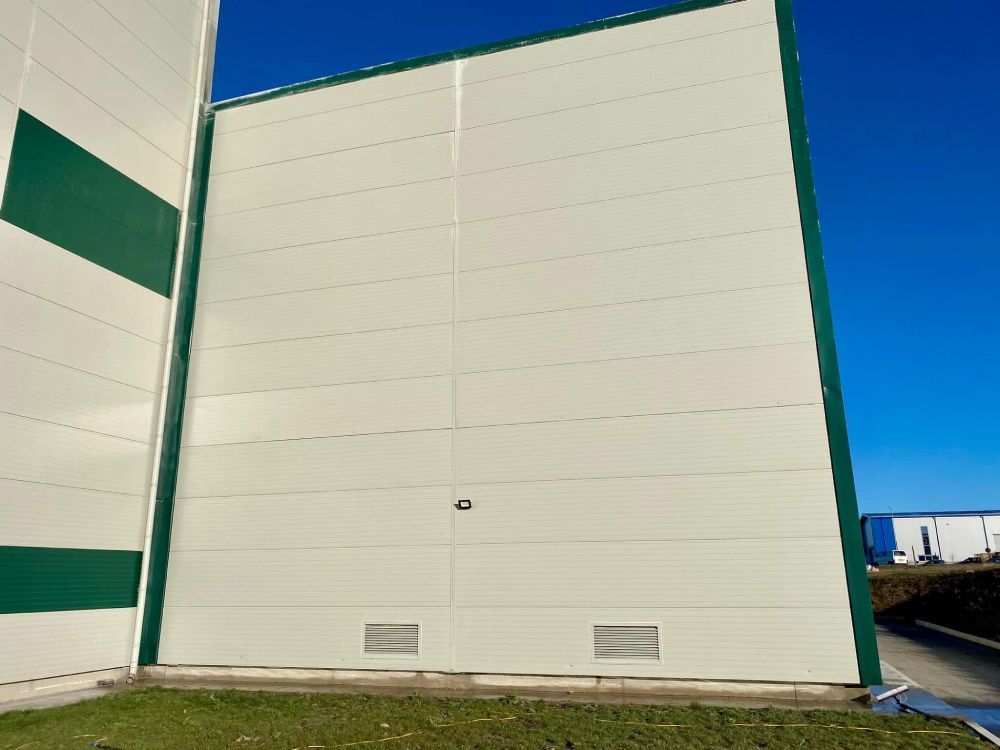 Weiße Industriegebäudewand mit grünen Zierelementen unter blauem Himmel, von der Seite gesehen.