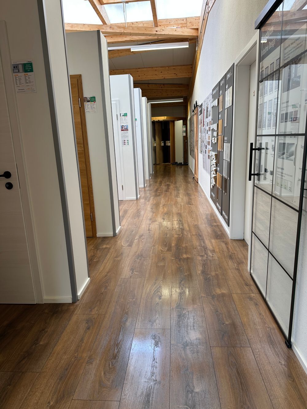 Langer Flur mit Holzboden, Oberlichtern, Türen und Wandvitrinen in einem büro- oder galerieartigen Gebäude.