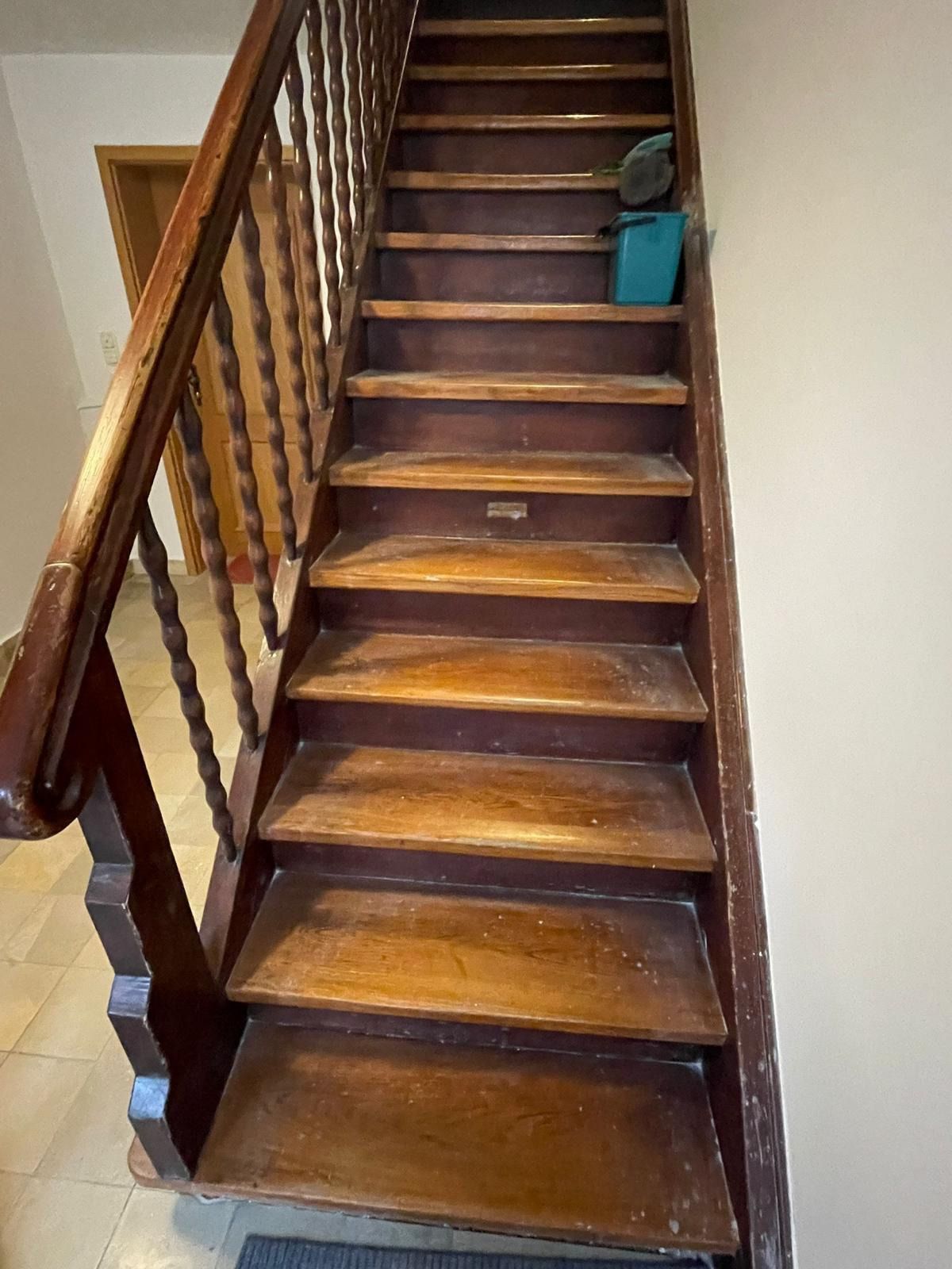 Holztreppe mit braunen Stufen und Geländer, ein blauer Eimer in der Nähe des oberen Endes, in einem schmalen Flur.