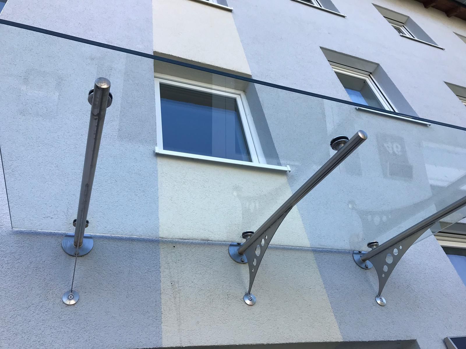 An der hellgrauen Gebäudefassade unterhalb der Fenster sind metallene Stützarme an der Wand befestigt.
