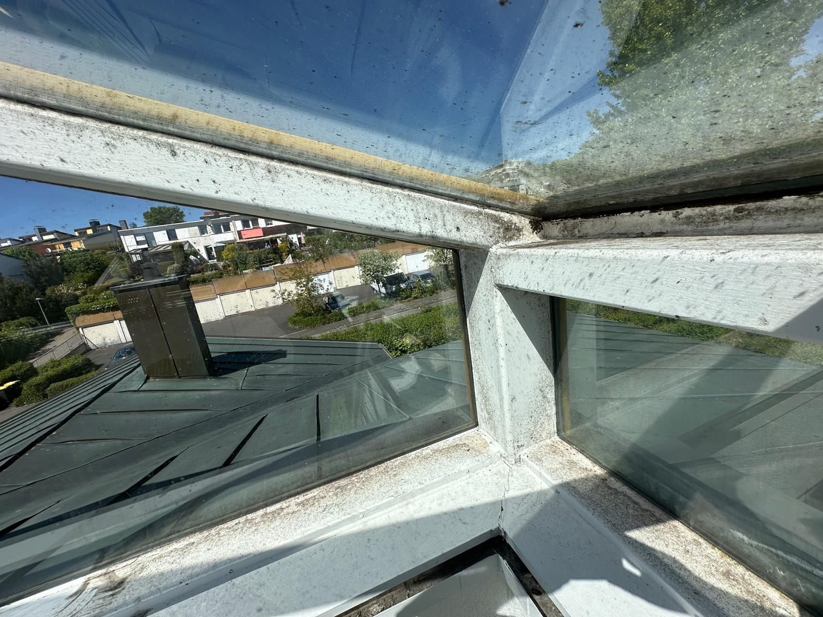 Blick aus einem Fenster über Dächer, Häuser und blauen Himmel an einem Hang
