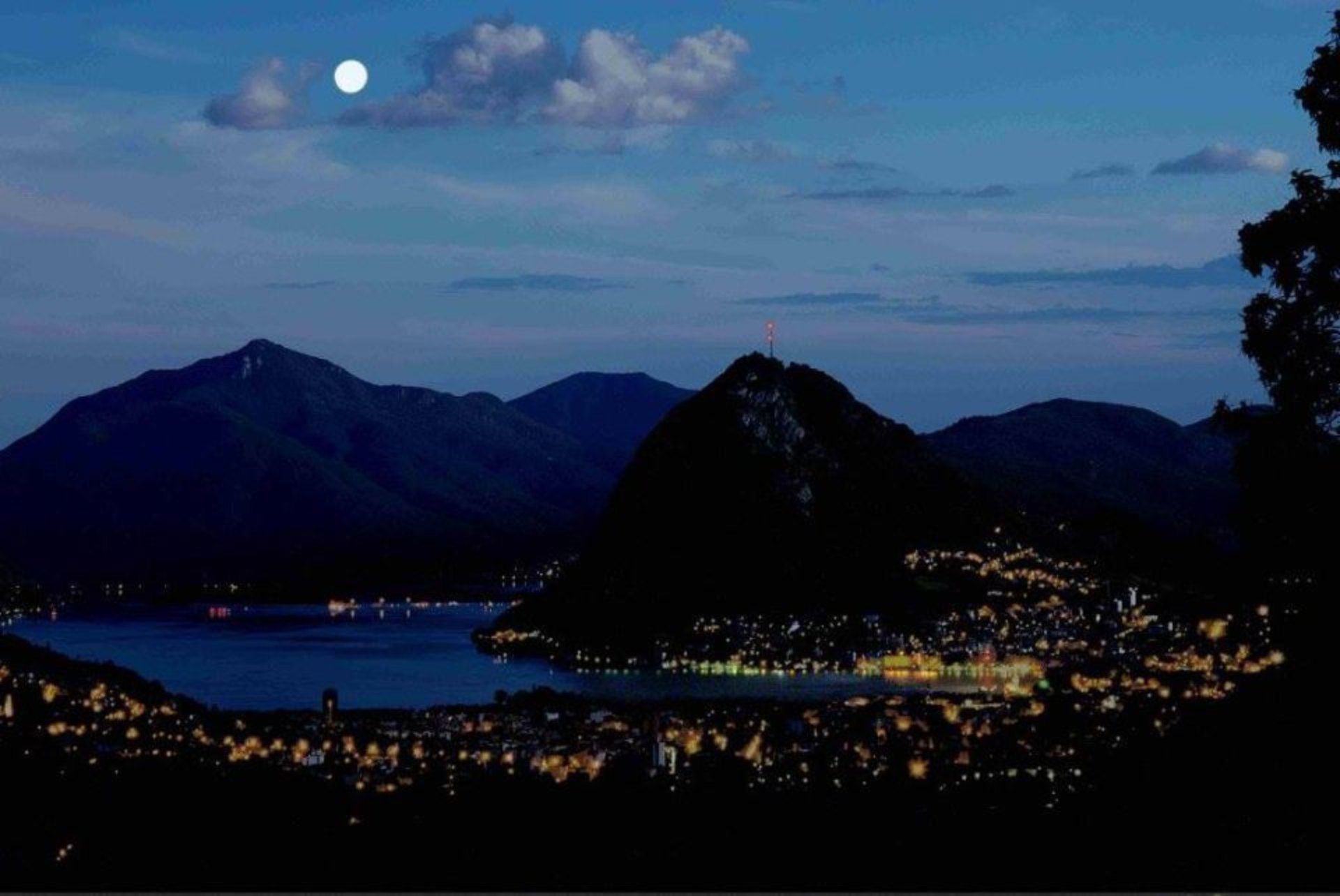 Una luna piena è visibile su un lago con le montagne sullo sfondo