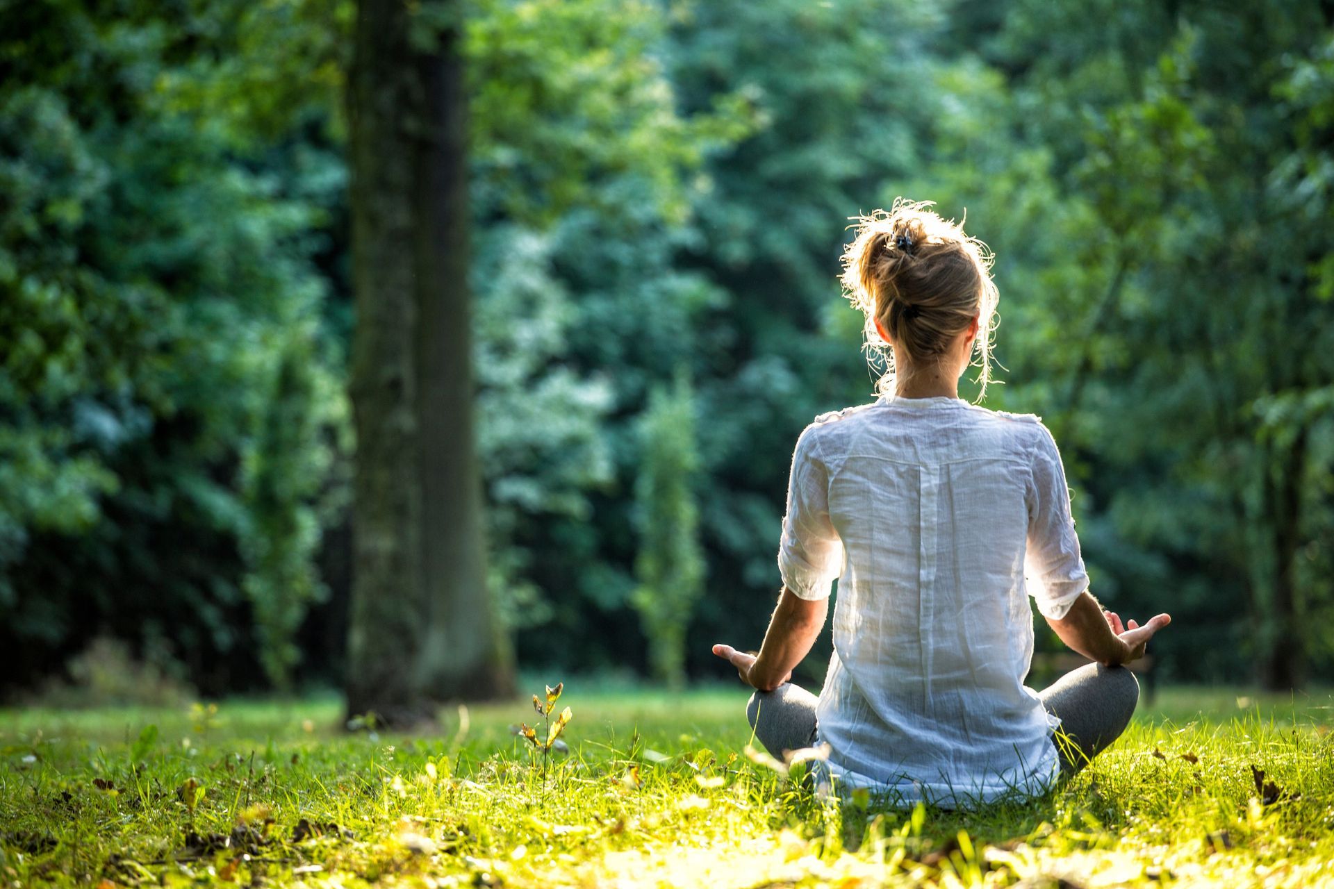 Femme méditant dans un parc, assise en tailleur, les mains jointes.
