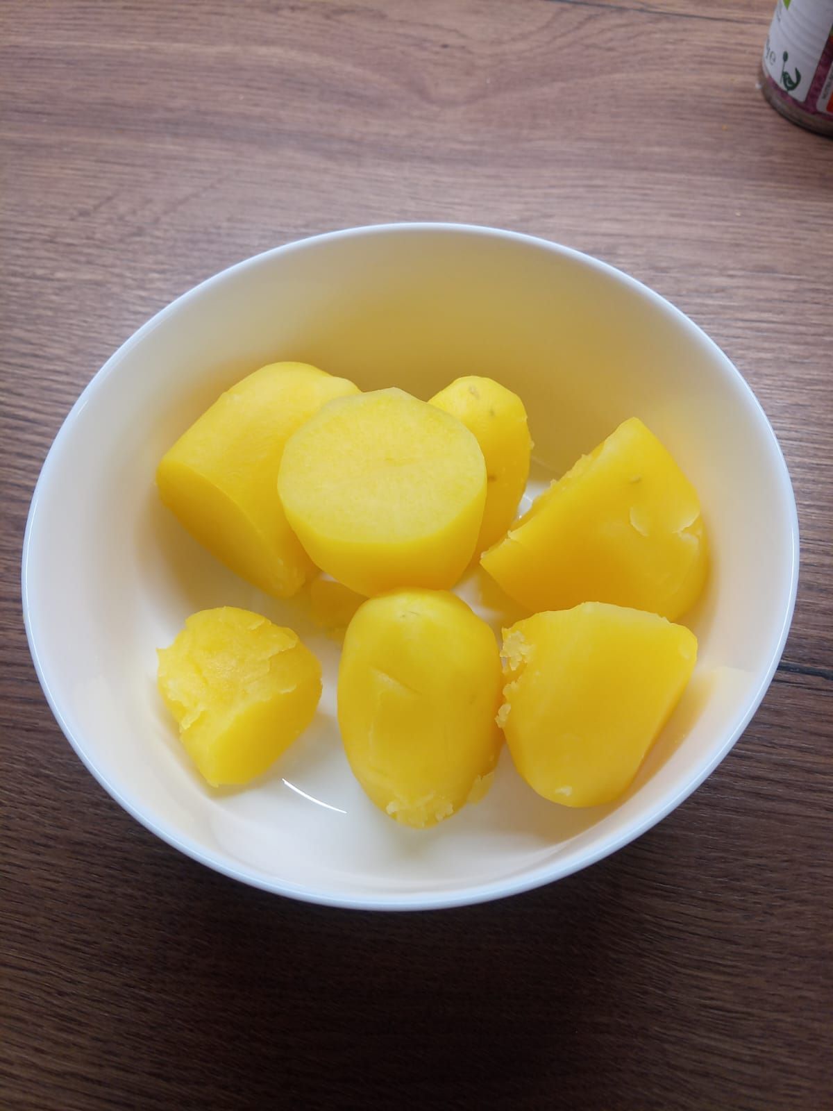 Eine weiße Schüssel gefüllt mit gelben Kartoffeln auf einem Holztisch