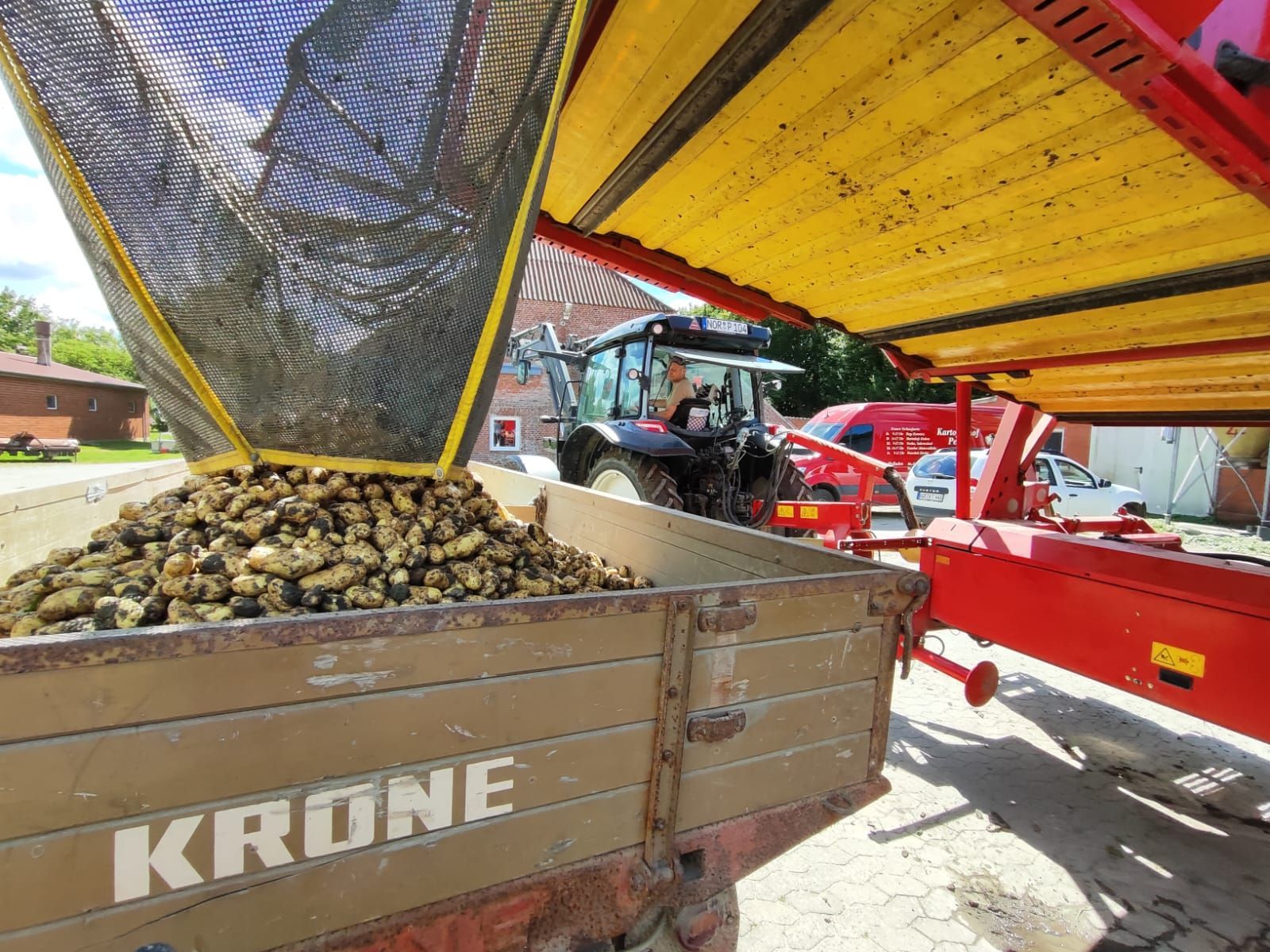 Ein Traktor lädt Kartoffeln in einen Krone-Anhänger.