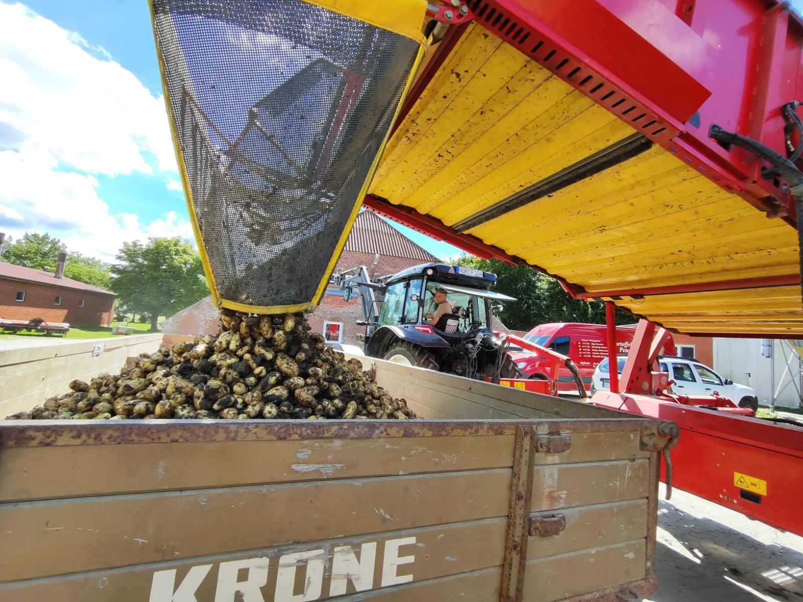 Ein Traktor schüttet Kartoffeln in einen Krone-Anhänger