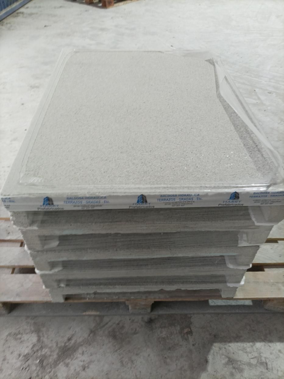 Pila de paneles rectangulares de color gris claro envueltos en plástico transparente sobre una paleta de madera.