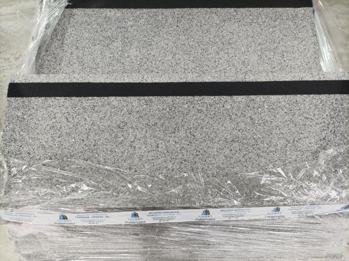 Peldaños de escalera, color gris claro con tiras de seguridad negras, envueltos en plástico transparente.