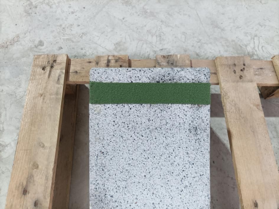 Muestra de piedra moteada de color gris con banda verde sobre palet de madera.