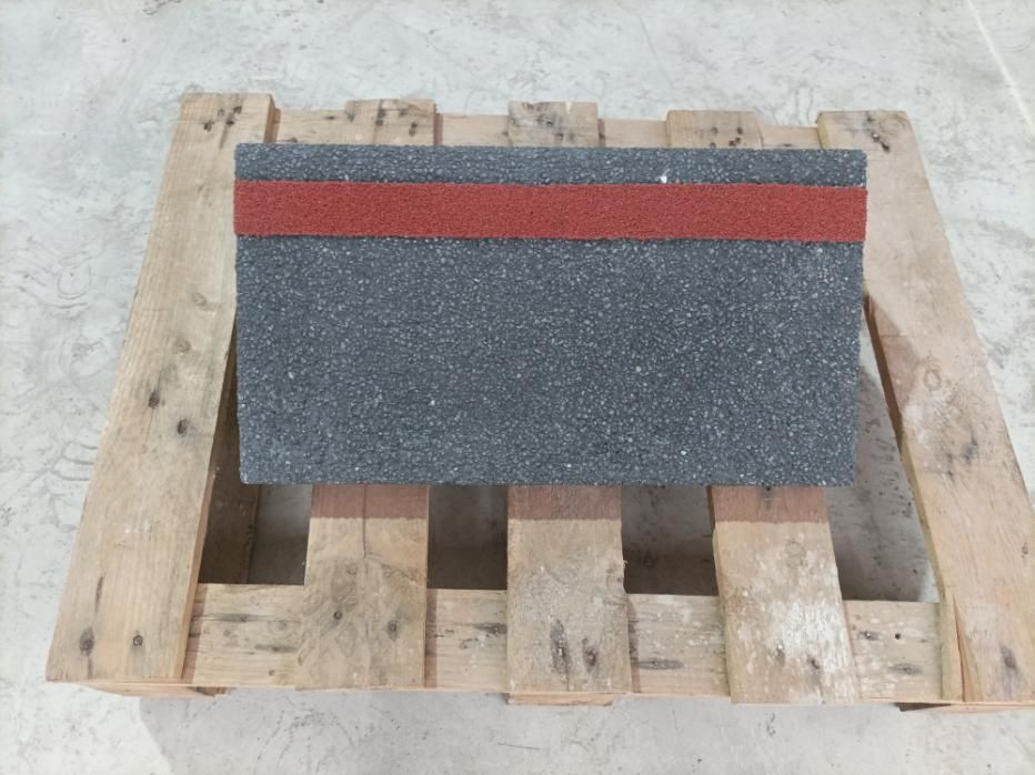 Piedra rectangular de color gris oscuro con una franja roja, apoyada sobre una plataforma de madera.