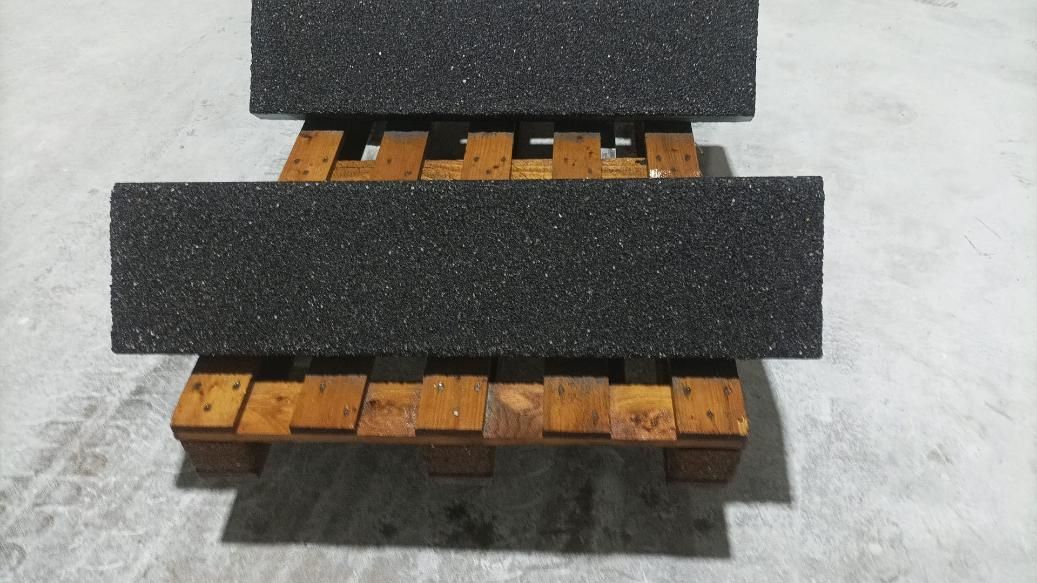 Dos rectángulos oscuros y texturizados sobre una pequeña paleta de madera sobre una superficie gris.