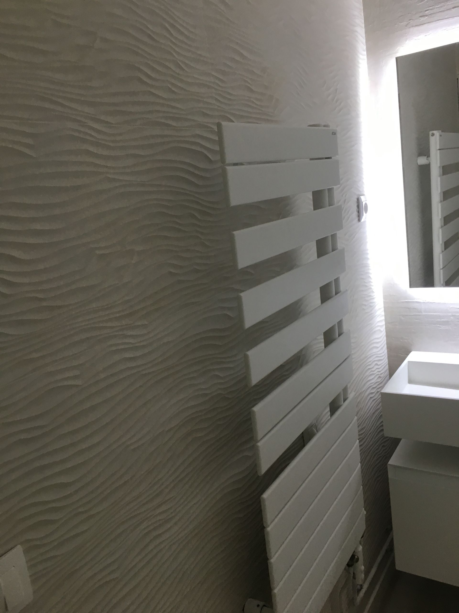 Sèche-serviettes blanc sur un mur blanc texturé dans une salle de bains moderne