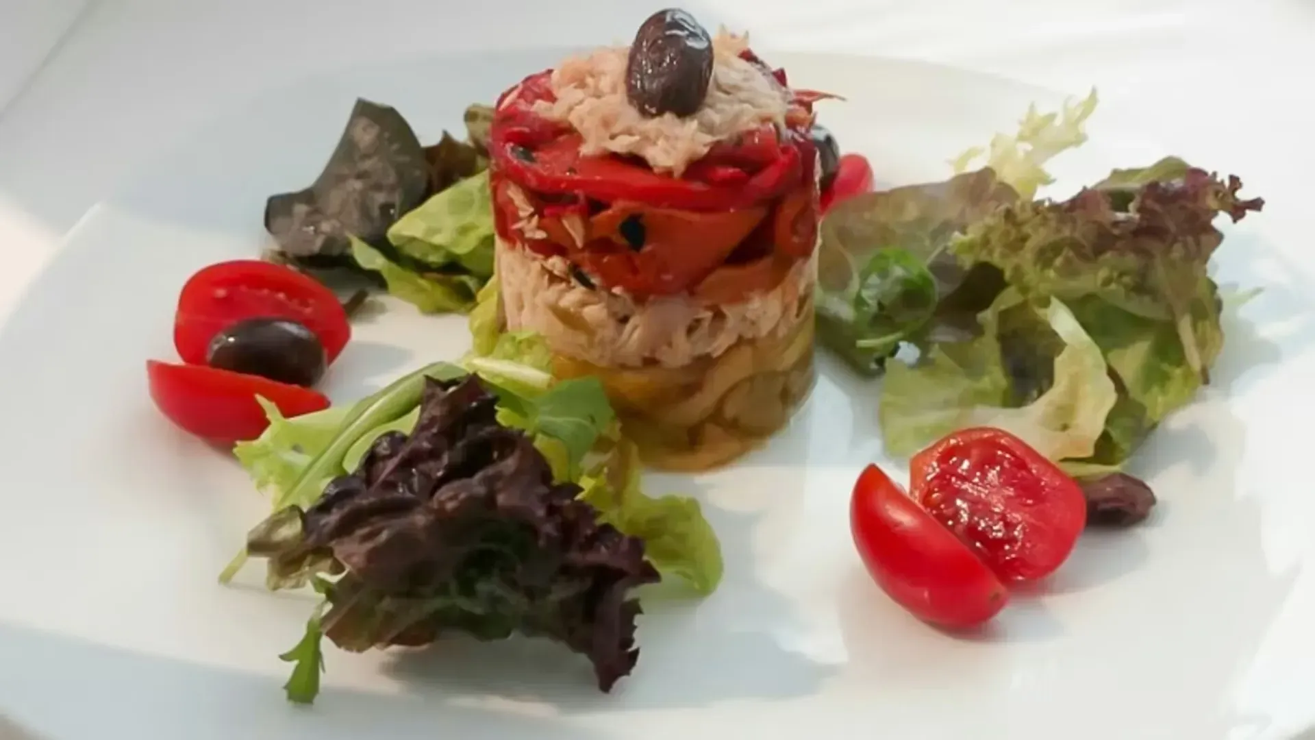Ensalada gourmet con capas de verduras, tomates cherry y hojas verdes variadas en un plato blanco.