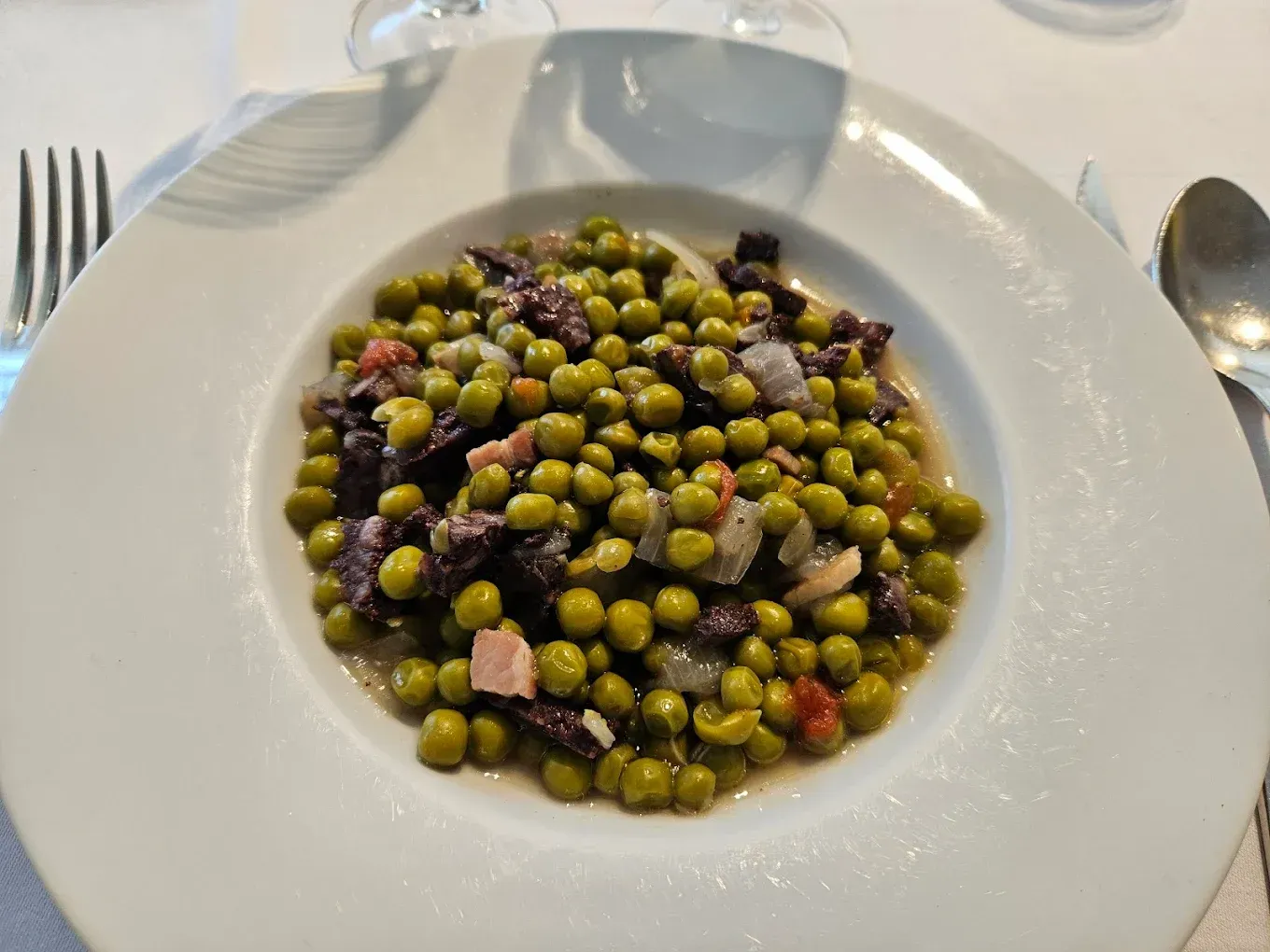 Plato blanco con guisantes verdes y carne en dados en salsa sobre una mesa de comedor.