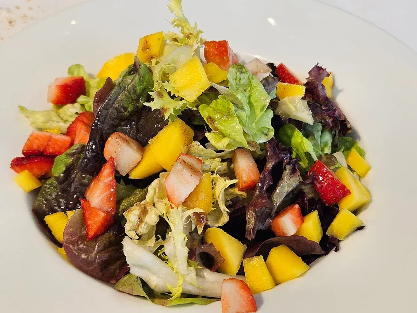 Ensalada de frutas variadas y hojas verdes de colores en un plato blanco.