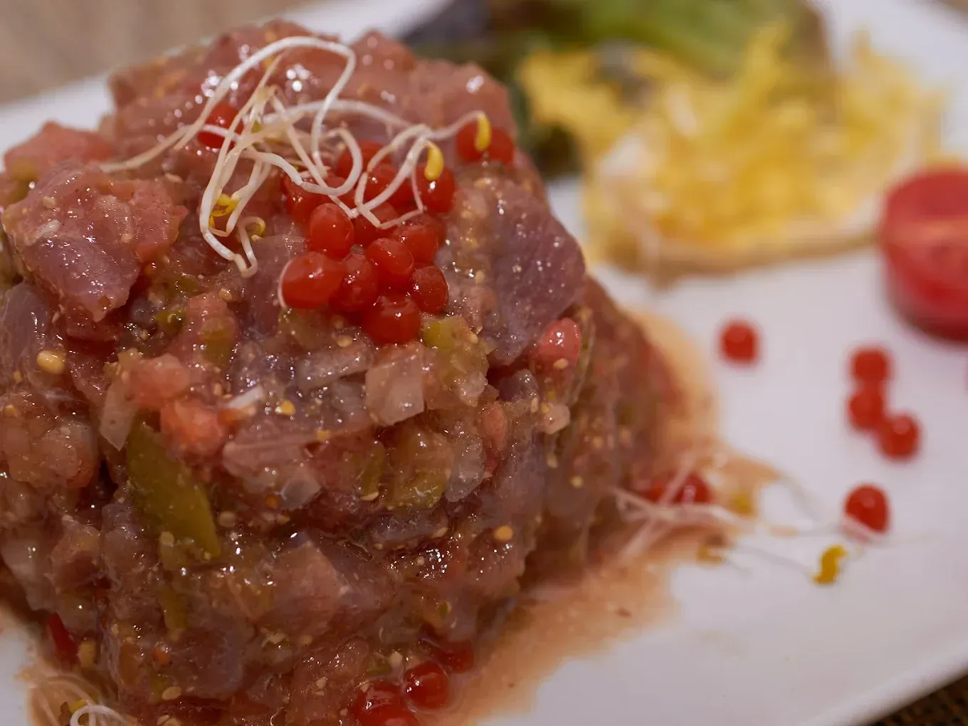 Tartar de atún gourmet cubierto con microvegetales y caviar rojo en un plato blanco.