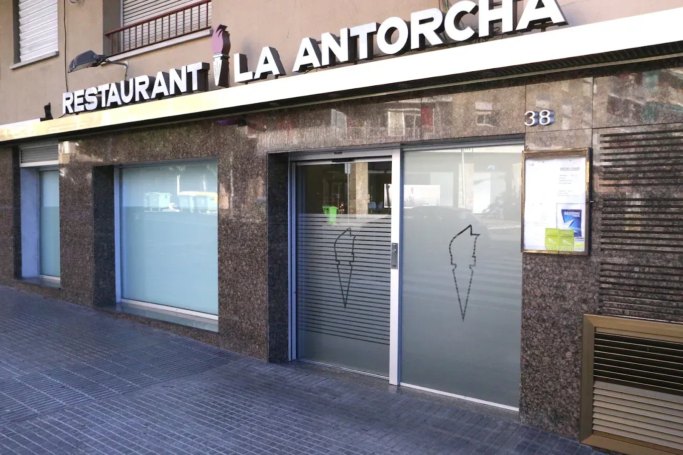 Vista desde la calle de la entrada del restaurante La Antorcha con puertas de cristal y fachada de ladrillo.