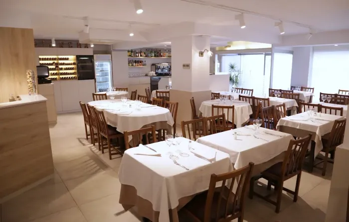 Comedor vacío de un restaurante con manteles blancos, sillas de madera e iluminación interior cálida.
