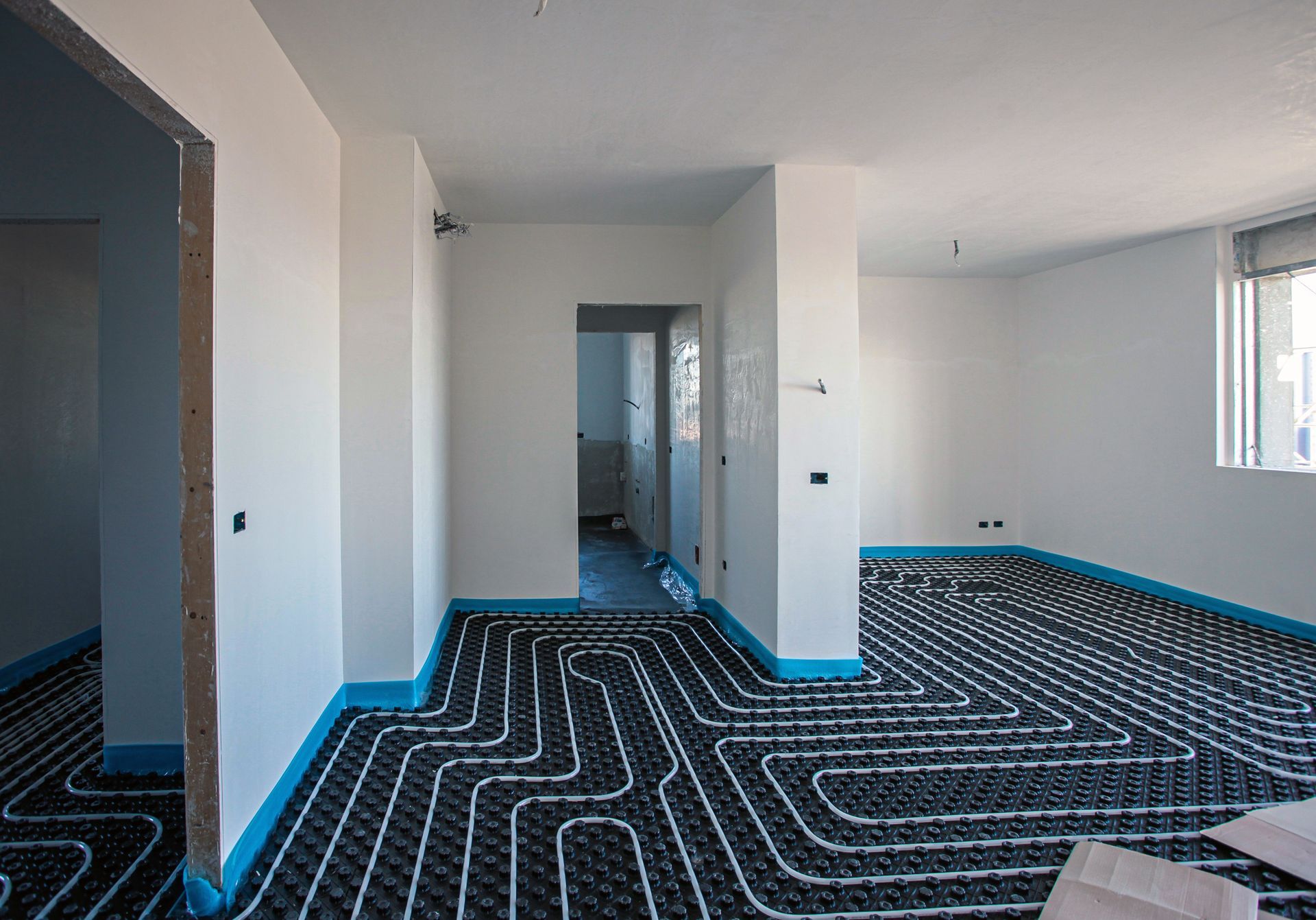 Pièce vide non meublée aux murs blancs et à la moquette noire à motifs bordée de bleu, vue depuis une porte