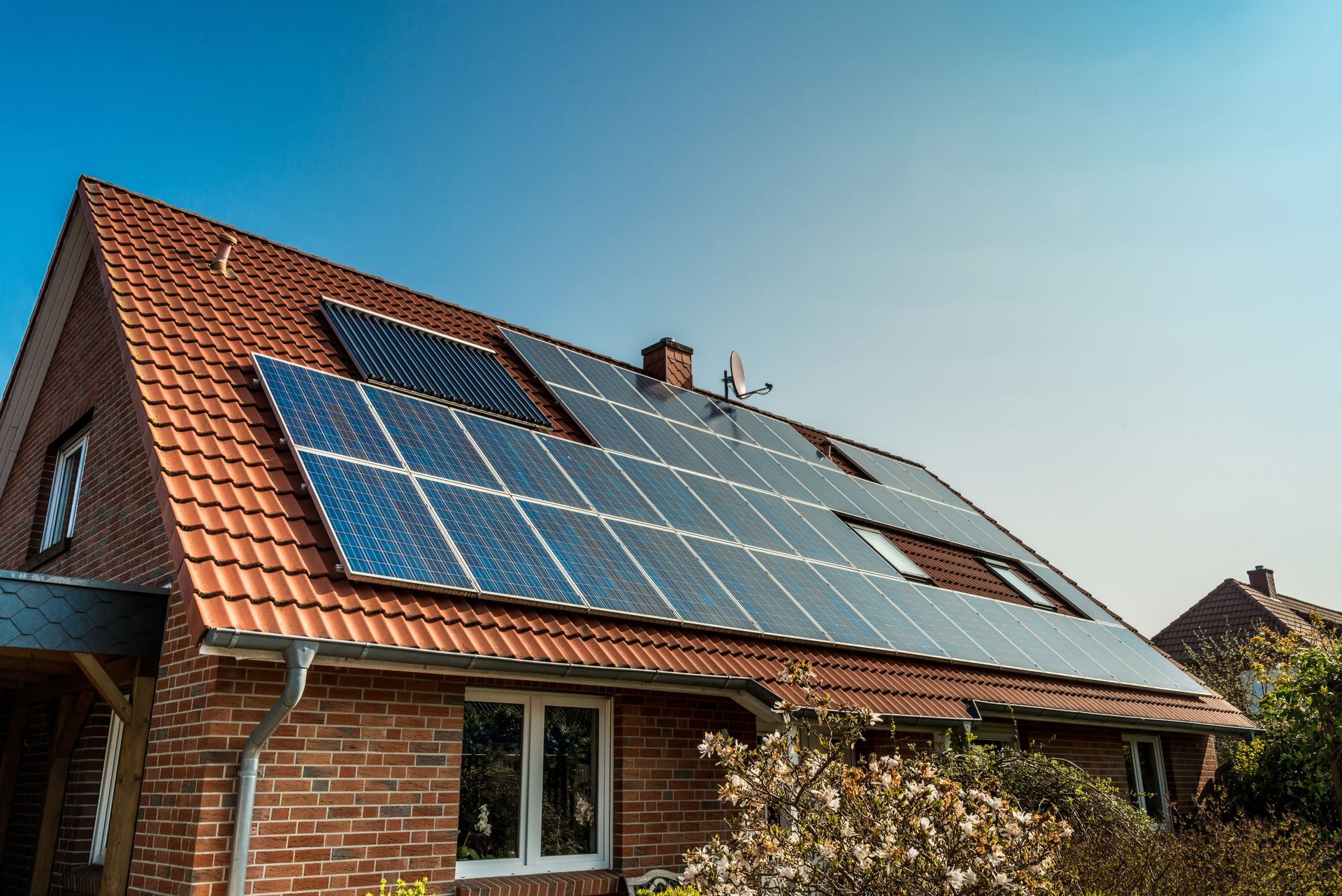 Maison en briques avec panneaux solaires sur un toit rouge en pente sous un ciel bleu clair