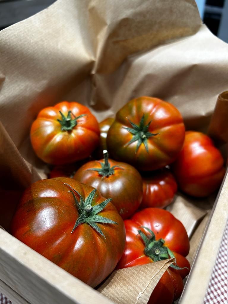 Una caja de madera llena de tomates envueltos en papel marrón