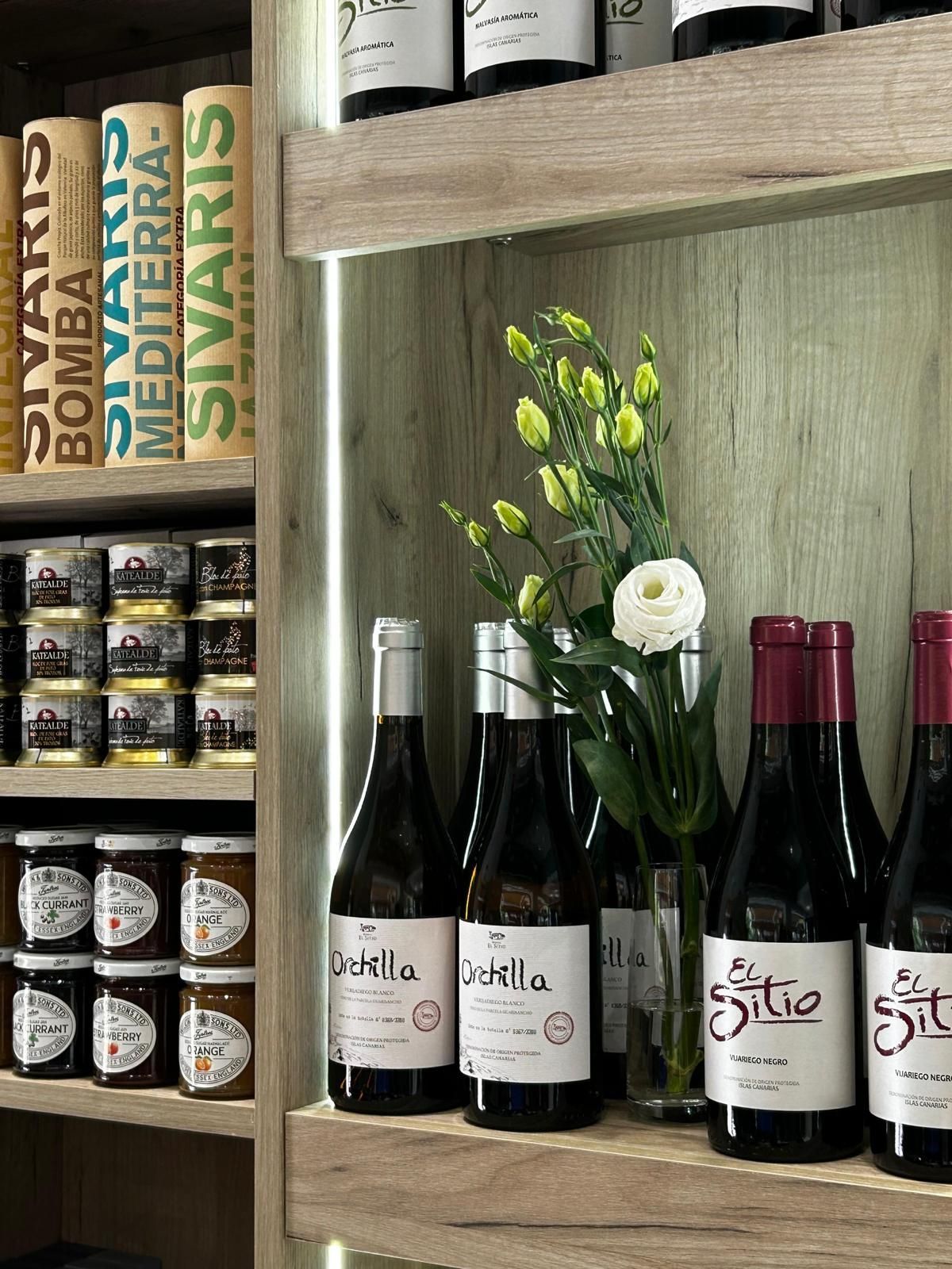 Un estante lleno de botellas de vino y un jarrón con flores.