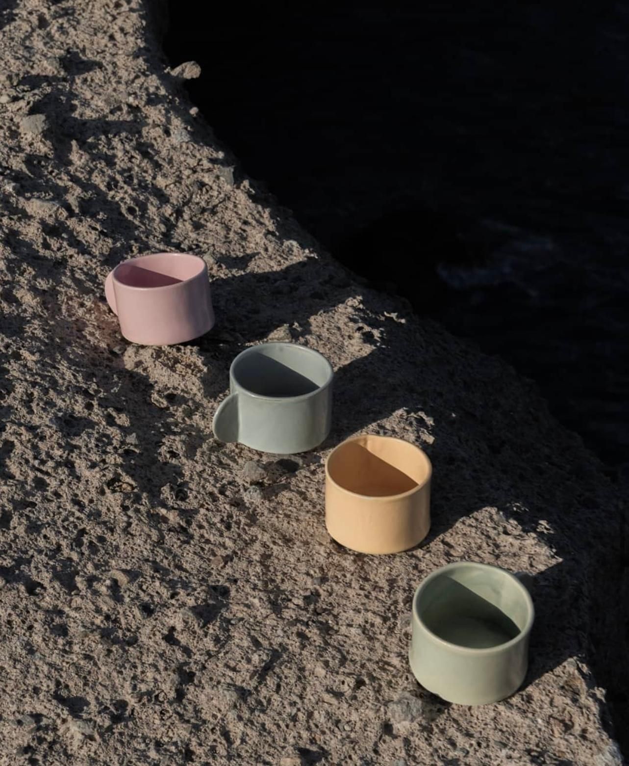 Cuatro tazas de diferentes colores están sobre una playa de arena.