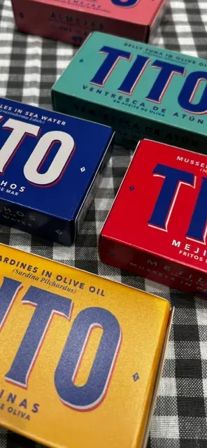 Sobre un mantel a cuadros reposan cuatro cajas de sardinas tito en aceite de oliva.