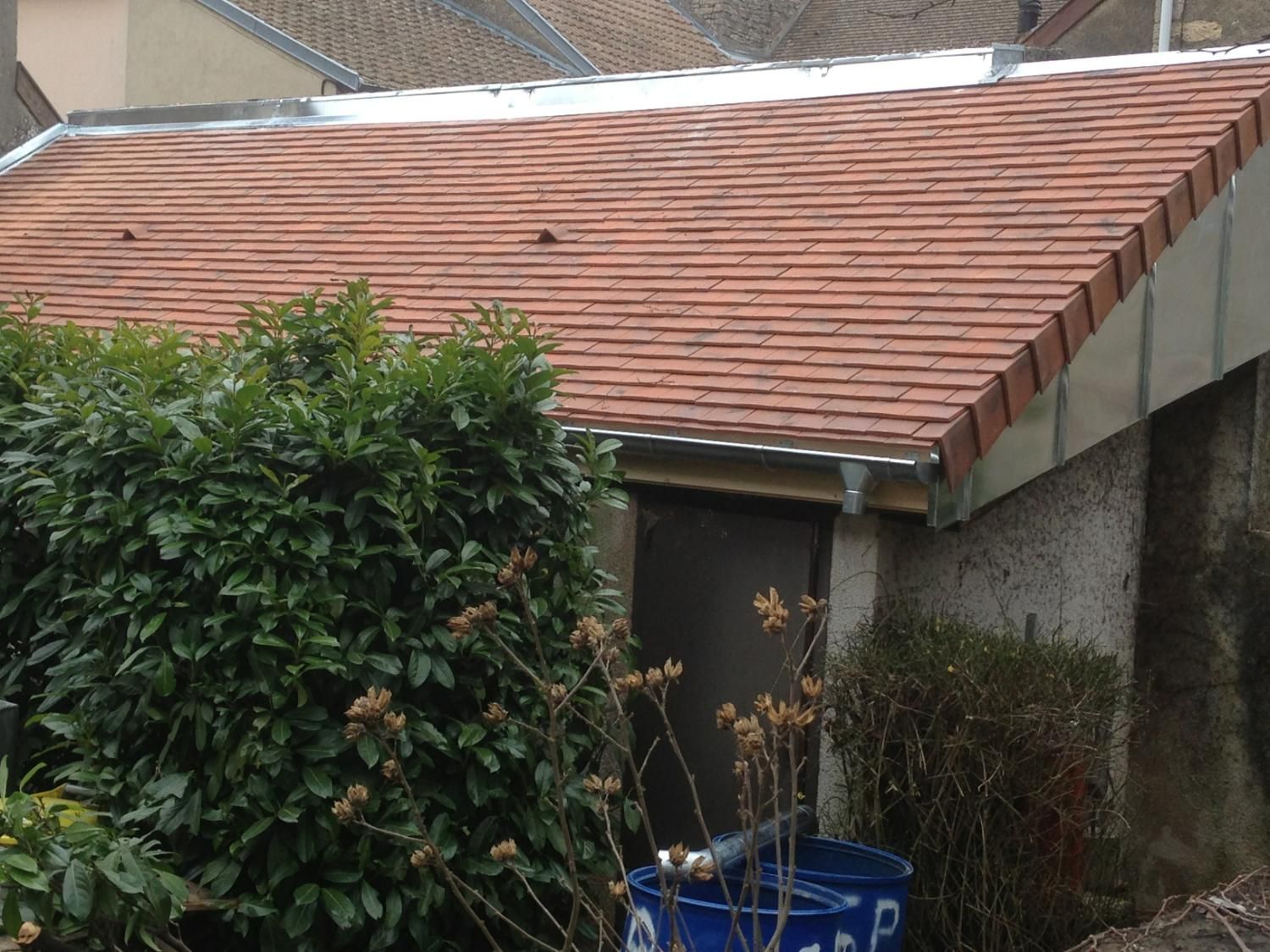 Un petit bâtiment au toit de tuiles rouges, avec un buisson vert au premier plan.