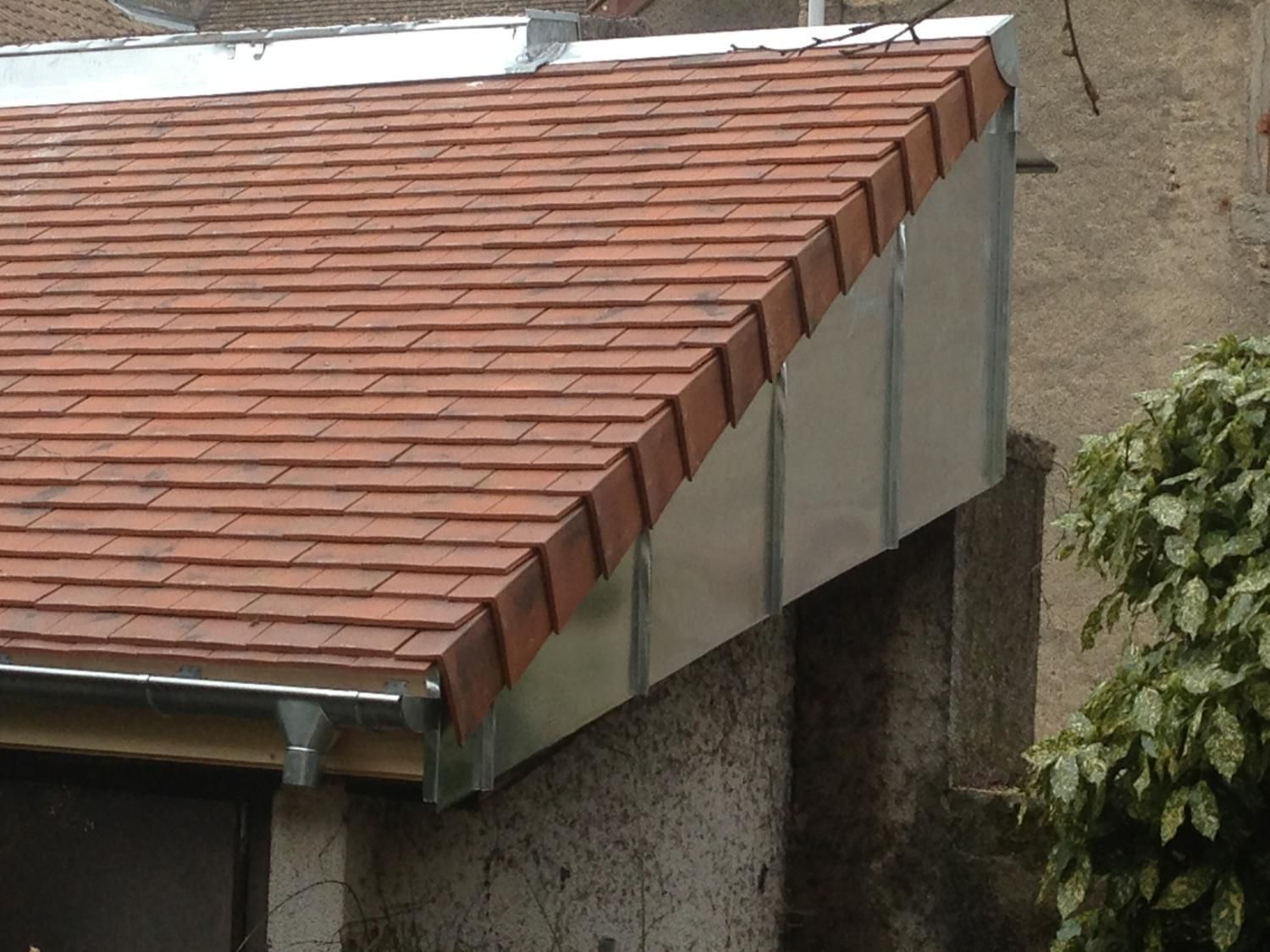 Toiture en tuiles de terre cuite avec solins métalliques sur la façade d'un bâtiment.