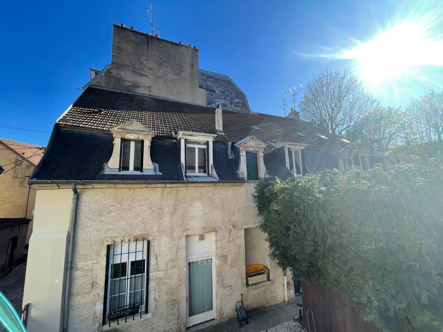 Bâtiment en pierre au toit sombre, avec des lucarnes et un ciel ensoleillé.