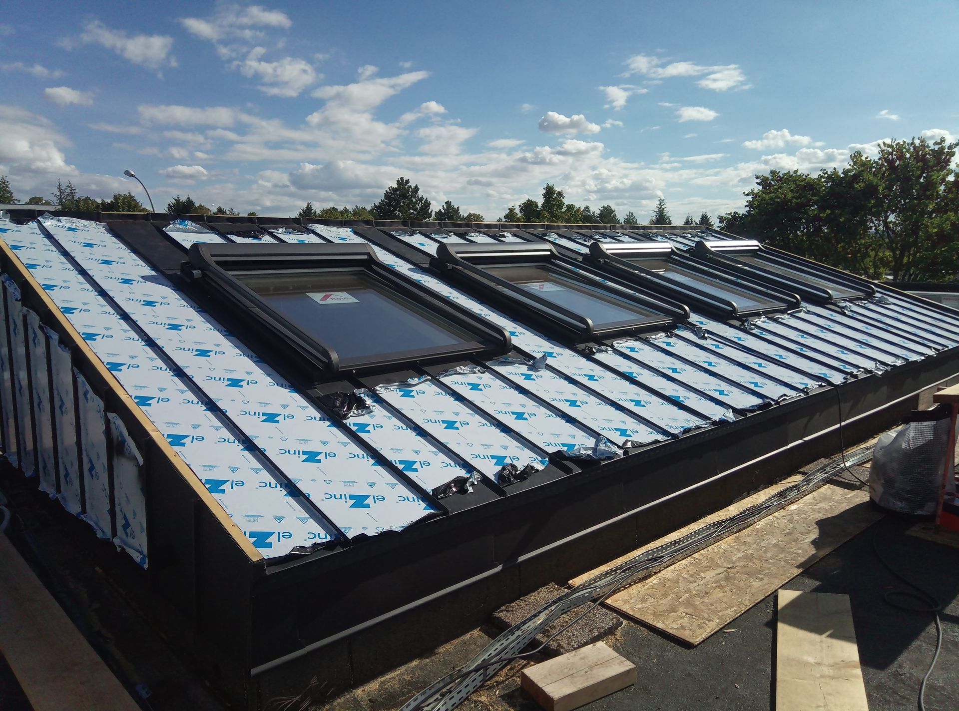 Un toit plat partiellement terminé avec des puits de lumière sous un ciel bleu.