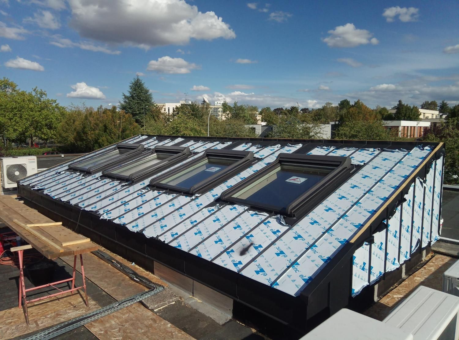 Un toit métallique avec trois puits de lumière en construction par une journée ensoleillée.