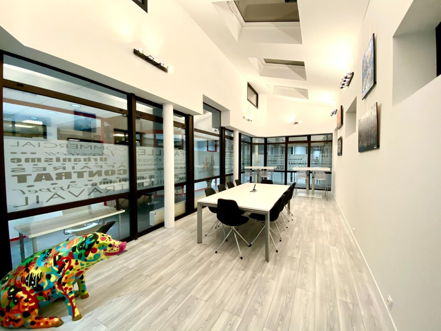 Espace de bureau moderne avec une grande table de conférence, des fenêtres et une statue de chien colorée.