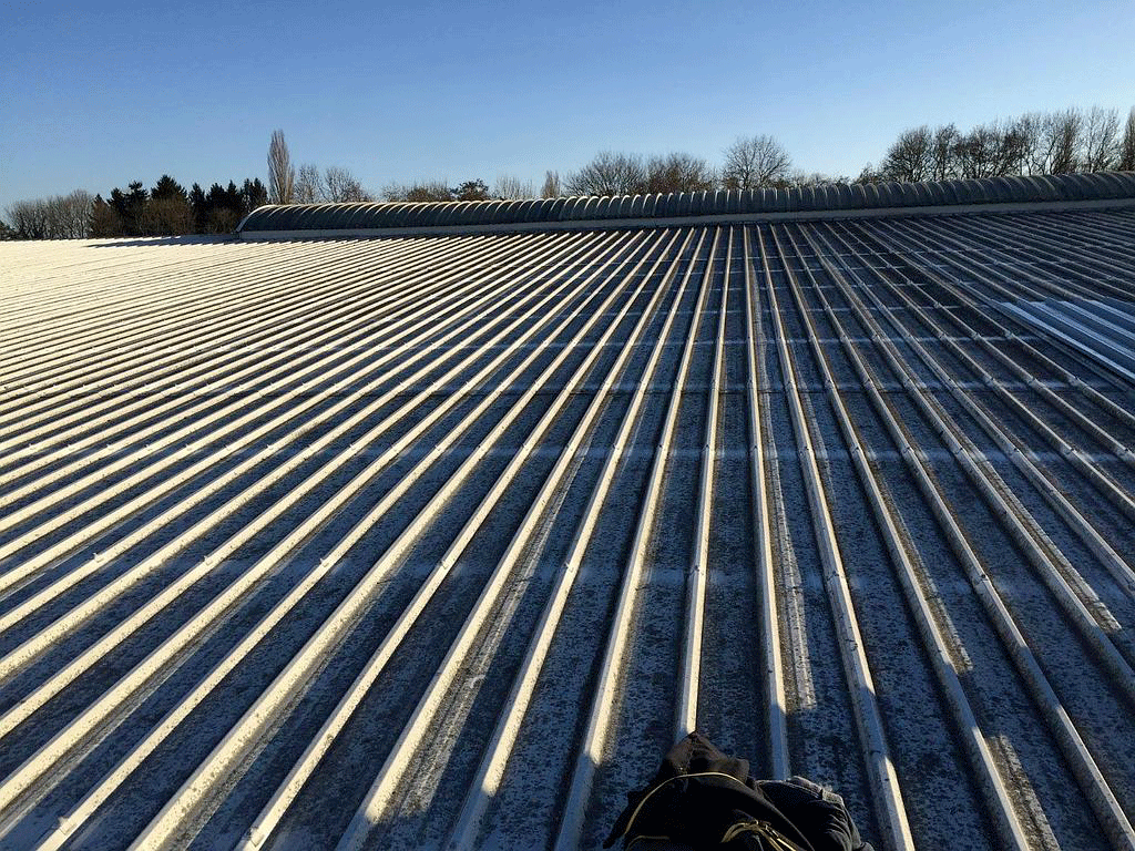 Un toit en tôle ondulée, peut-être enneigé, s'étend jusqu'à l'horizon, sous un ciel bleu clair.