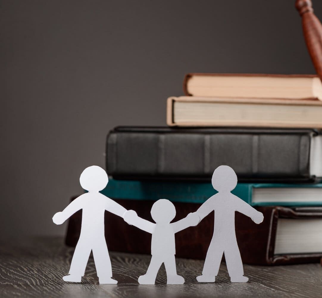 Tres personas de papel tomadas de la mano frente a una pila de libros
