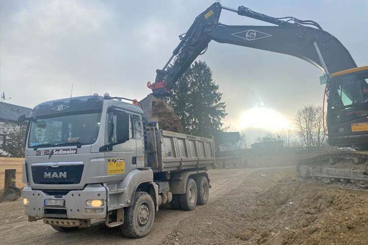 Auf einer Baustelle lädt ein Bagger Erde in einen Muldenkipper der Anton Sedlmaier GmbH.
