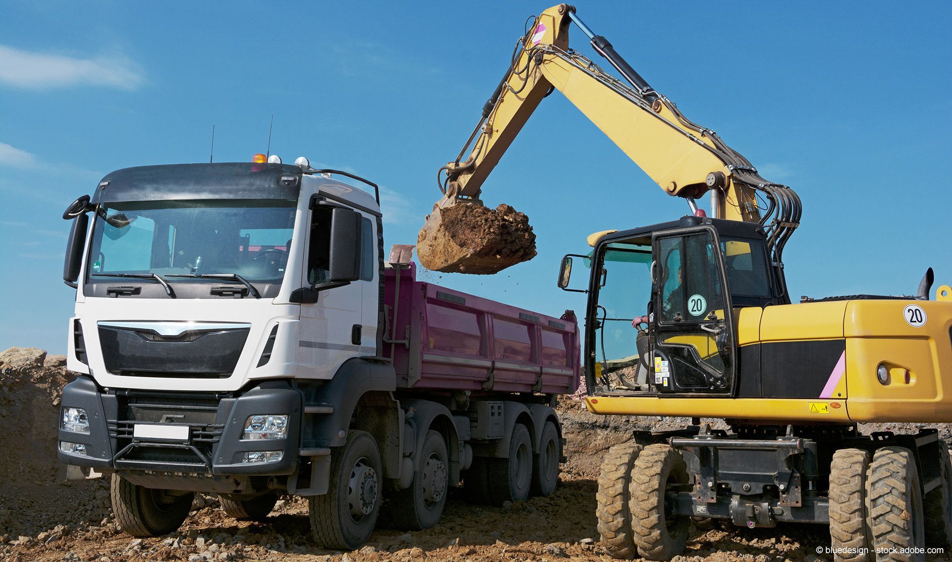 Ein gelber Bagger verlädt auf einer Baustelle Erde in einen weiß-roten Muldenkipper.