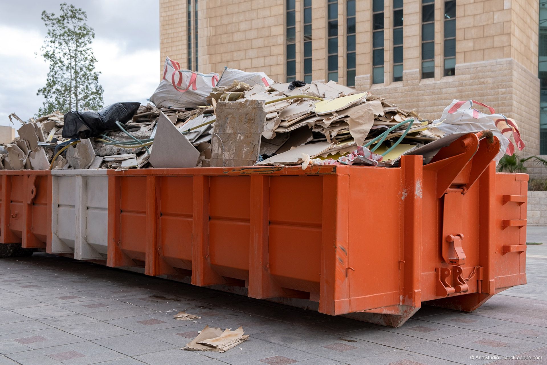 Ein orange-weißer Schuttcontainer mit Bauabfällen vor einem Gebäude.