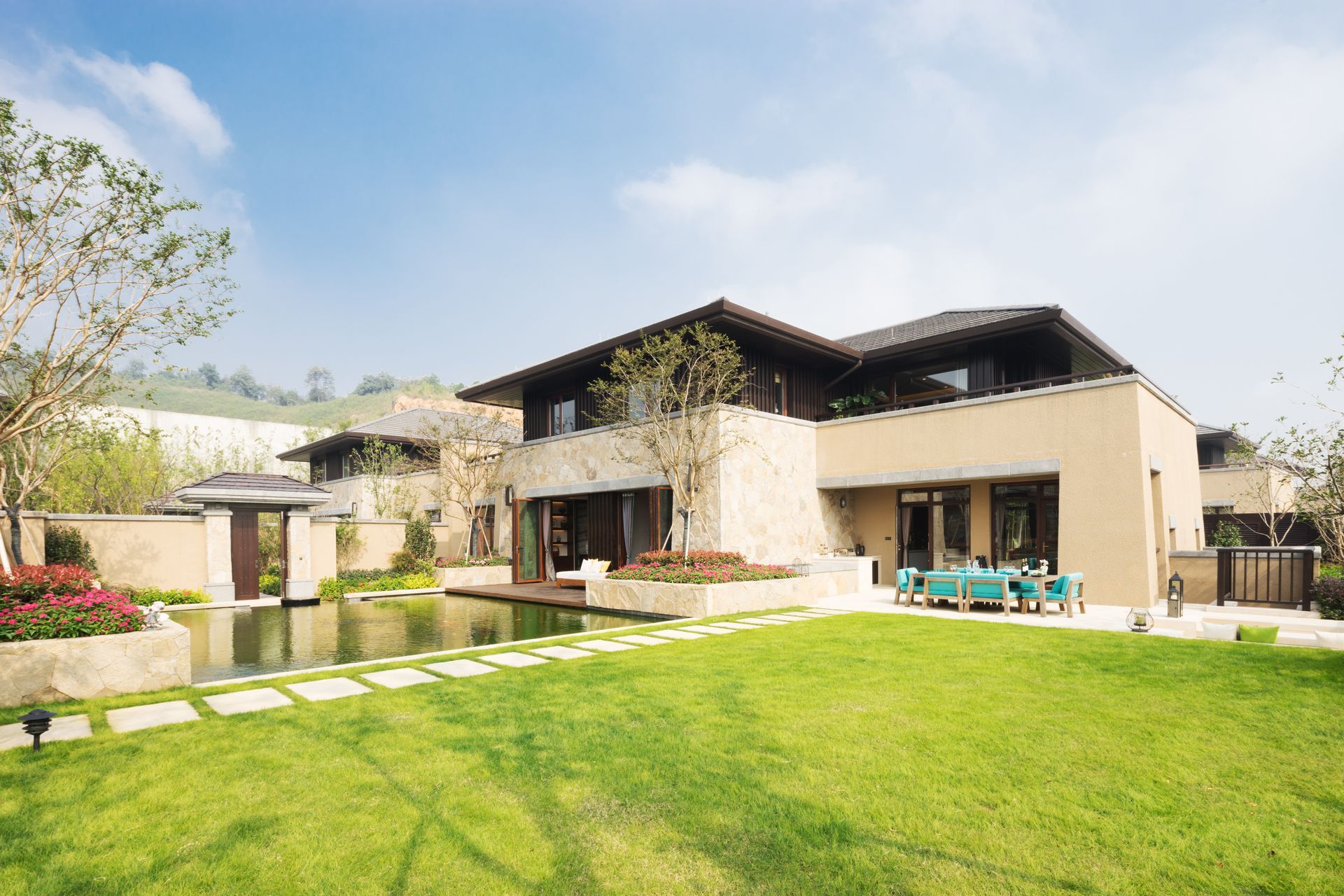 Maison beige moderne avec une grande pelouse verte, un patio et un ciel d'un bleu éclatant