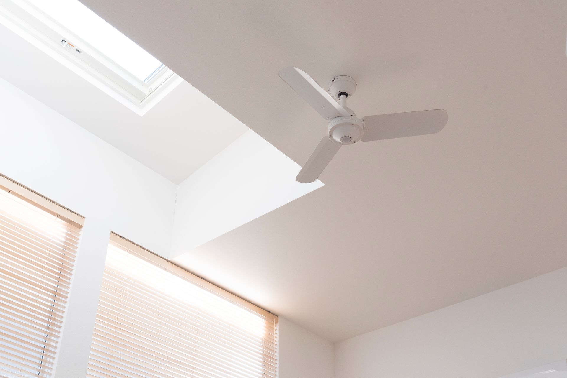 Plafond blanc avec ventilateur et puits de lumière au-dessus des stores
