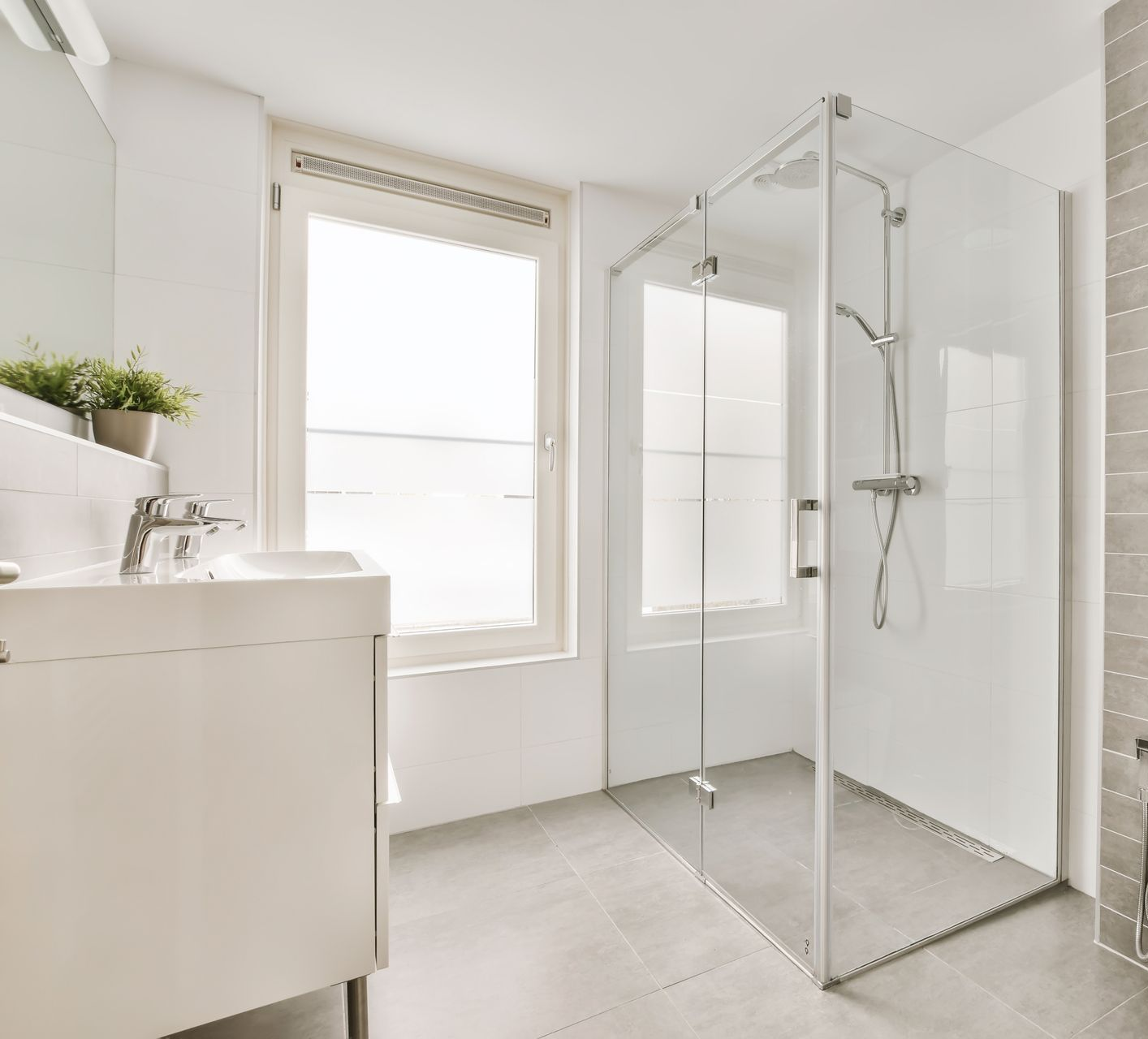 Salle de bain blanche lumineuse avec cabine de douche en verre, fenêtre et meuble-lavabo