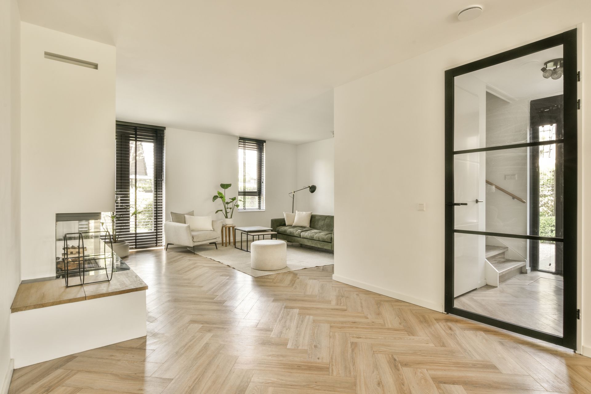 Salon minimaliste lumineux avec parquet à chevrons, murs blancs et grandes portes vitrées à cadre noir