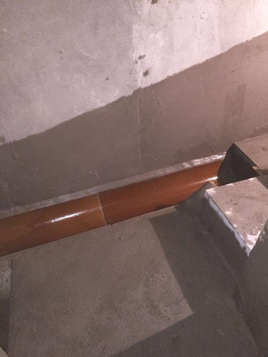 Una tubería marrón reposa sobre un piso de concreto al lado de una escalera.