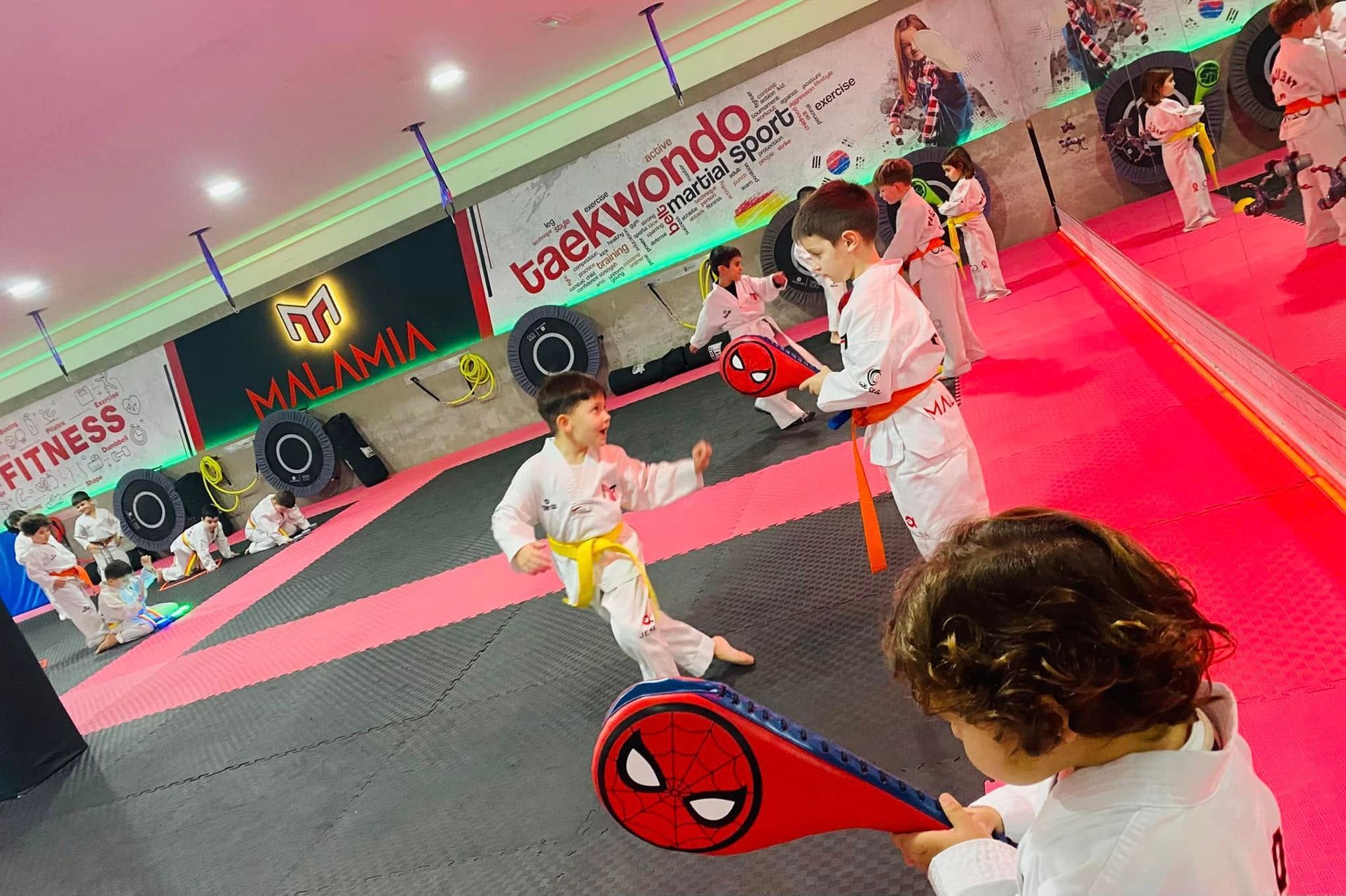 Niños con uniformes blancos de artes marciales sobre una colchoneta roja en un gimnasio cubierto