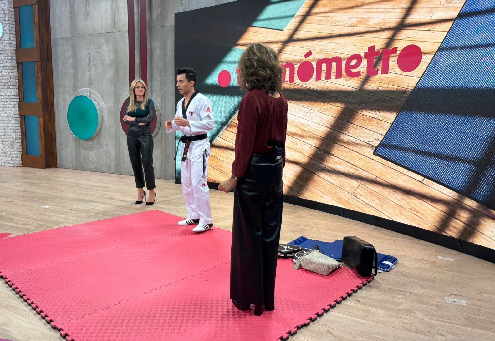 Dos personas practicando patadas de artes marciales en un gimnasio; una sostiene una almohadilla y la otra golpea.