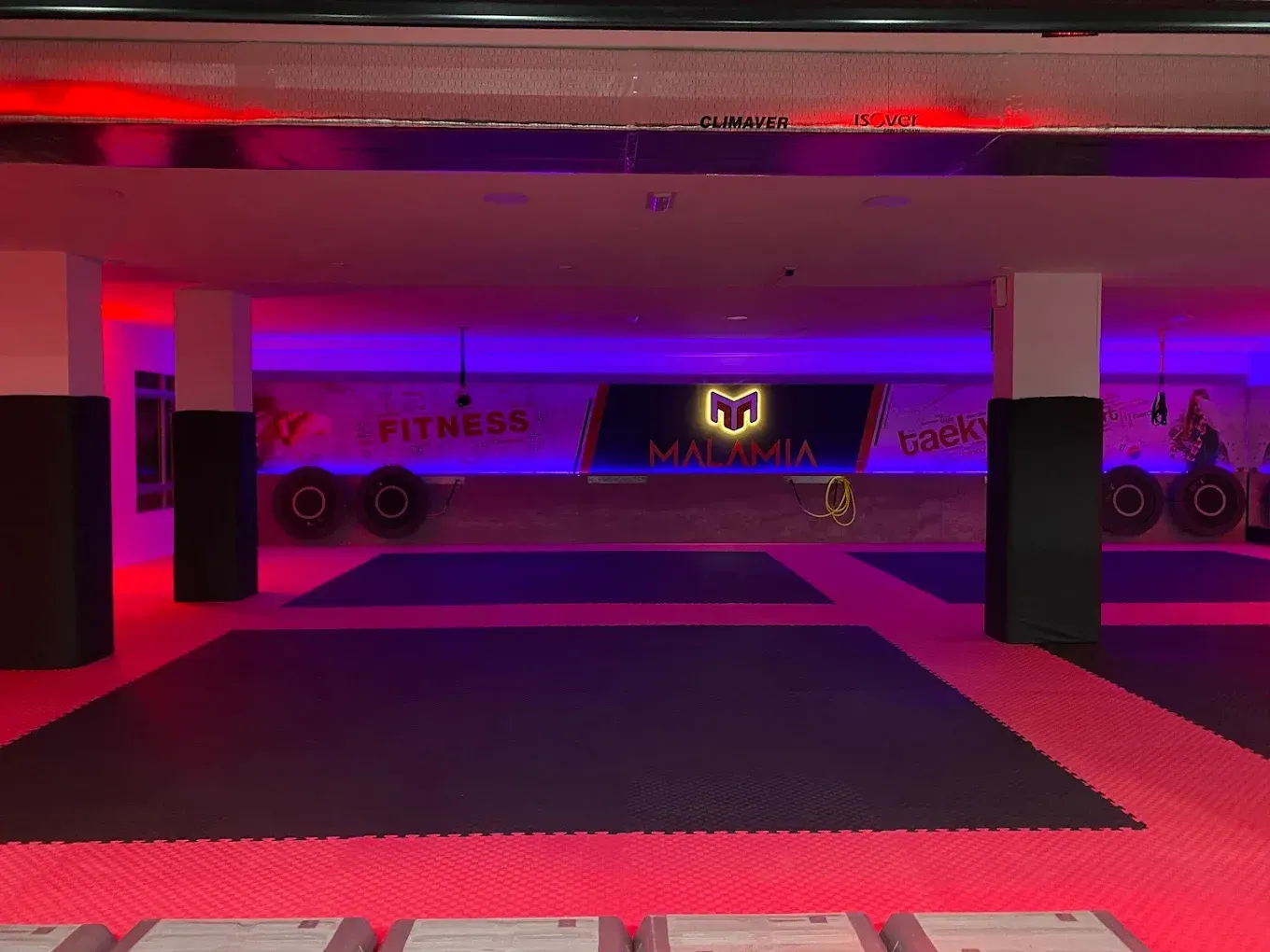 Gimnasio vacío con iluminación de color rojo púrpura y grandes colchonetas en el suelo.
