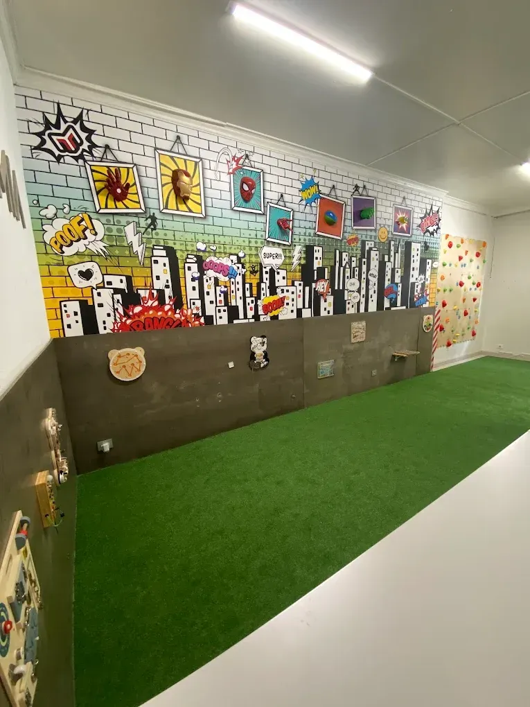 Hoyo de minigolf interior lleno de color, con césped verde, murales y obstáculos en el lado izquierdo.