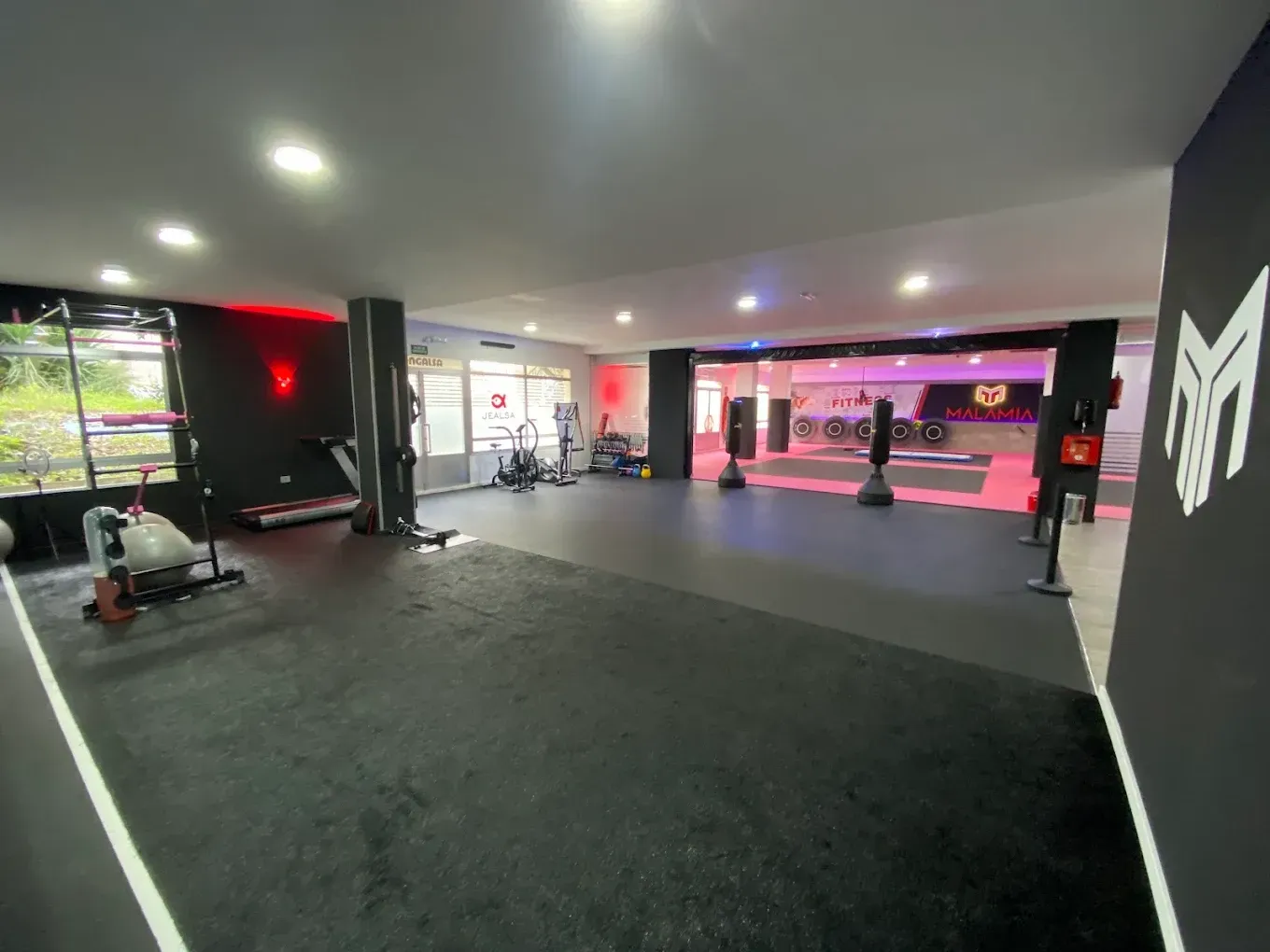 Gimnasio vacío con suelo negro, pared con espejos e iluminación de acento roja dentro de un estudio moderno.