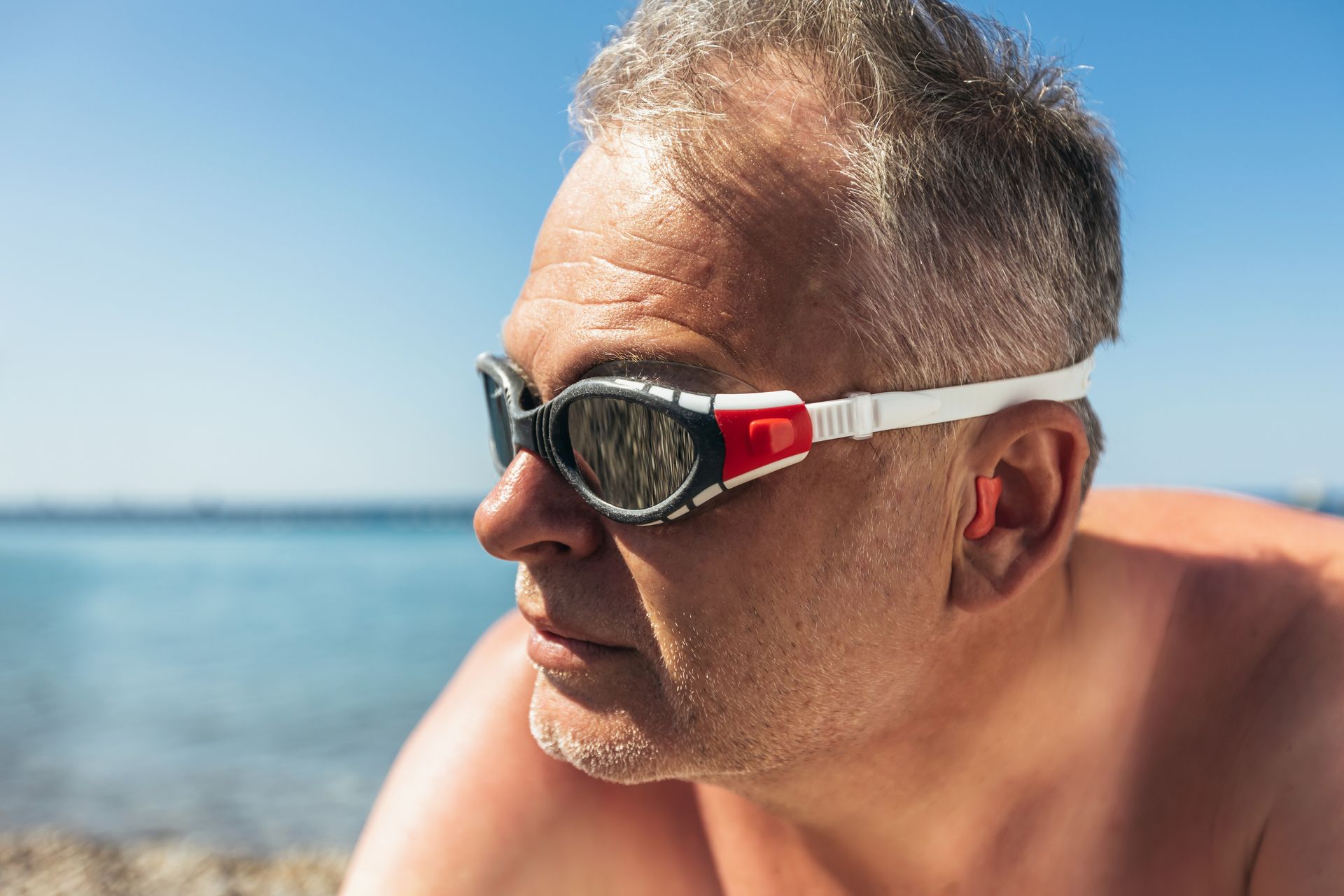 Un homme à la plage porte des lunettes de piscine et des bouchons d'oreilles